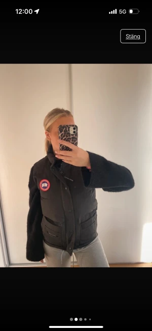 Svart dunväst från Canada Goose - Svart dunväst från Canada Goose med klassisk logga på bröstet och stora fickor framtill. Västen har hög krage, knappar och dragkedja. Perfekt för lager-på-lager och riktigt snygg till hoodie eller stickad tröja.