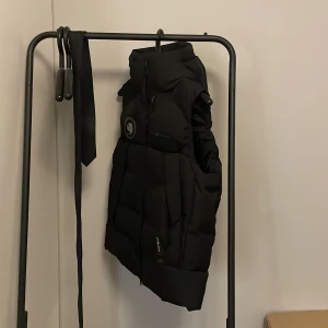 Svart dunväst från Sail Racing M - Svart dunväst från Sail Racing i storlek medium. hög fodrad krage och quiltad med dragsko vid halsen. Oanvänd, legat i garderoben ett tag nu känner att jag vill bli av med den så pris kan diskuteras.