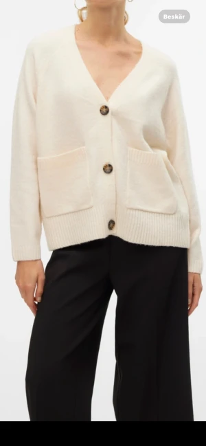 Beige kofta från vero Moda - Mysig beige kofta med v-ringning och stora knappar framtill. Koftan har två rejäla fickor och ribbade muddar vid ärmslut och nederkant. Perfekt för lager-på-lager och chill dagar. Passar dig som gillar enkel och clean stil. 