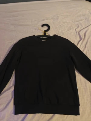 Svart basic tröja från H&M - En stilren svart basic tröja från H&M i storlek 146/152. Tröjan har rund hals, långa ärmar och är tillverkad i mjuk bomull. Perfekt för dig som gillar enkel och clean stil. Passar dig som vill ha en klassisk look.