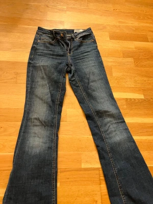 Blå bootcut jeans från Vero Moda - Snygga blå jeans från Vero Moda med klassisk bootcut-modell. Jeansen har fem fickor, dragkedja och knapp framtill samt coola slitningar för en avslappnad look. Tillverkade i jeansmaterial med kontrastsömmar och en mörkblå tvätt.