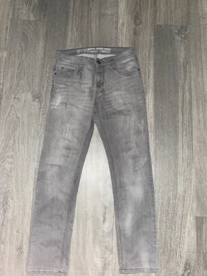 Grå jeansbyxor från Elveroy - Snygga grå jeansbyxor från Elveroy med klassisk femficksdesign och subtila slitningar framtill. Byxorna har rak passform och normal midja, tillverkade i mjukt jeanstyg som ger en cool och avslappnad vibe. Perfekta för dig som gillar stilrena och neutrala färger.