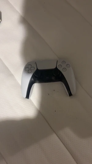 PlayStation 5 DualSense Controller - Snygg och modern PlayStation 5 DualSense-kontroll i vitt och svart. Kontrollen ser ut att vara i gott skick med minimalt slitage. Perfekt för dig som vill ha en extra handkontroll till din PS5. Alla knappar och spakar syns tydligt och ser hela ut.