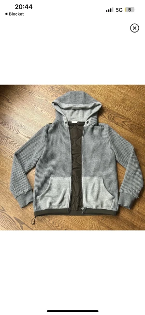 Grå quiltad hoodiejacka från Moncler - SKICK ÄR 9/10. Snygg grå hoodiejacka från Moncler med quiltad mörkgrön front och rygg. Jackan har huva, två stora fickor och dragkedja hela vägen. Ärmar och huva är stickade i grått, medan kroppen är fodrad och quiltad för extra värme. Perfekt för kyliga dagar. 