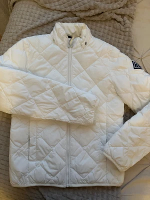 Vit quiltad pufferjacka från Gant - Vit pufferjacka från Gant med quiltat mönster och hög krage. Jackan har avtagbar huva och Gant-logga på ärmen. Den är köpt på barnavdelningen i storlek 146/152 motsvarar XS. Använd fåtal gånger & är i mycket bra skick!❄️🩵