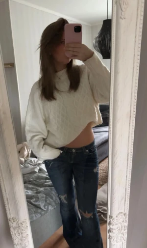 Vit croppad stickad tröja - Säljer en vit croppad stickad tröja med kabelstickat mönster och rund hals. Tröjan har lång ärm och är perfekt för dig som gillar en chill och trendig look. Passar snyggt till jeans eller kjol.