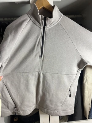 Ljusgrå Sail Racing fleece-tröja - Ljusgrå fleece-tröja från Sail Racing med hög krage och half zip framtill. Tröjan har långa ärmar, två fickor med dragkedja och diskret Sail Racing-logga på ärmen och ryggen. Perfekt för kyliga dagar och riktigt skön att ha på sig.