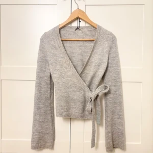 Grå korta Gina tricot (omlott/rosett)🎀 - Grå kofta från Gina Tricot med omlott och rosett vilket gör att man kan dra ut banden hur man vill. Beroende på om man vill ha midjan mer ”tight” eller ”lose”. Har använt max 2 gånger och den är aldrig tvättad så inte nopprig!🍒❣️