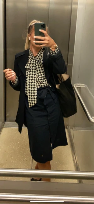 Kjol NA-KD - Mörkblå kostymkjol med knappar, slits på ena sidan och knytning i midjan. Knappen längst ner har tyvärr lossnat, men går enkelt att sy fast igen. Skickar självklart med den! I övrigt fint skick!