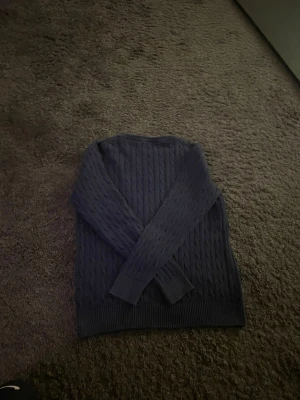 Mörkblå kabelstickad tröja från GANT - Säljer en mörkblå kabelstickad tröja från GANT med rund halsringning och broderad logga på bröstet. Tröjan har långa ärmar och ribbade muddar vid ärmslut och nederkant. Perfekt för dig som gillar klassisk och stilren look. Perfekt nu inför vintern!❄️🥃