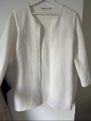 Vit cardigan jacka från ONLY - Säljer en stilren vit cardigan jacka från ONLY i storlek S. Jackan har långärmad design och är tillverkad i ett ribbat, mjukt material som ger en skön känsla. Öppen framtill utan knappar eller dragkedja, perfekt för lager-på-lager och chill stil.