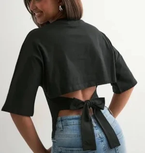 Svart topp med rosett - Säljer en svart croppad topp med halvlånga ärmar och snygg öppen rygg som knyts med en stor rosett baktill. Toppen har en enkel, stilren design och är gjord i ett mjukt bomullsmaterial. Perfekt för dig som vill ha en cool och trendig look. Från Nelly i stl xs, jättebra skick