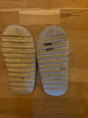 Beige slides med ribbad sula - Säljer ett par beige slides med bred rem över foten och kraftigt ribbad sula. Skorna har en chunky design och är tillverkade i syntetmaterial. Perfekta för sommaren och enkla att glida i och ur.