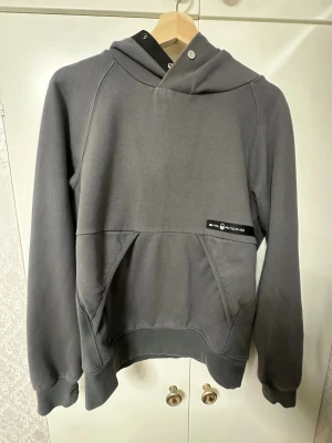 Grå hoodie från Sail Racing (säljs inte längre) - Snygg grå hoodie från Sail Racing med logga på bröstet och på huvan. Tröjan har en stor känguruficka framtill, ribbade muddar och coola detaljer vid halsen. Materialet är en mix av bomull och återvunnen polyester, vilket gör den både mjuk och hållbar. Jag har använt den 2 gånger men insåg snabbt att den va för liten på mig. Denna produkt säljs inte längre då pris kan diskuteras. (Kan ej fraktas) (Stockholm) 