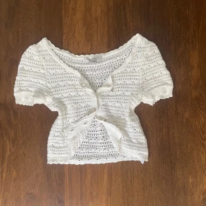 Vit stickad blus från Amisu - Supersöt vit stickad blus från Amisu med korta ärmar och rund hals. Blusen har ett ribbat mönster med små hål och knappar. Stickad i mjukt material för extra komfort. 