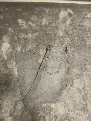 Gråa jeans Jack and Jones  - Säljer ett par grå jeans från Jack & Jones, modell Relaxed/Chris. De har en avslappnad passform med raka ben och klassisk femficksdesign. Jeansen är tillverkade i jeansmaterial och har en snygg tvättad look med ljusgrå ton. Perfekt för dig som gillar chill och stilren vibe. Skick 10/10 nypris 499kr säljs för 250kr pris kan diskuteras!