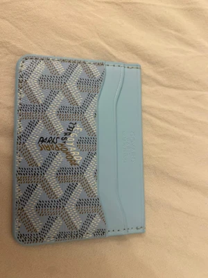 Ljusblå plånbok  - Supersnygg ljusblå plånbok med deras ikoniska grafiska mönster i beige och svart. Plånboken har flera kortfack och är tillverkad i skinn. Perfekt för dig som vill ha något stilrent och unikt i fickan.