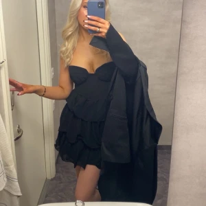 Svart volangklänning med hjärtformad urringning - Supersnygg svart kort klänning med hjärtformad urringning och volangkjol. Axelbandslös modell som ger en elegant och trendig look. Perfekt för dig som vill sticka ut och känna dig extra fin.