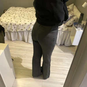 Grå kostymbyxor med bootcut - Snygga grå kostymbyxor med bootcut-snitt och hög midja. Byxorna har två knappar framtill och klassisk dragkedja. Passar perfekt för dig som gillar stilrena och tidlösa plagg med lite extra edge i siluetten.