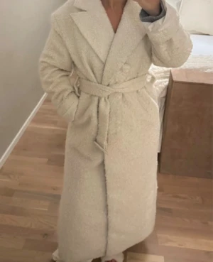 Beige kappa med bälte - Lång och  beige kappa med bred krage och bälte i midjan. Kappan har en oversized passform och är perfekt för kalla dagar. Stora fickor på sidorna och mjukt material som ger en mysig känsla🩷🩷