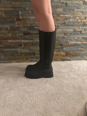 Svarta höga boots med chunky sula - Heej!🌸Säljer ett par svarta höga boots med chunky platt sula och rund tå. Skorna är tillverkade i syntetmaterial och har en minimalistisk design utan synliga detaljer. Perfekta för dig som vill ha en stilren och edgy look till höst och vinter. Köptes för ca 400 kr på Monki, använd vid två tillfällen.                            Hör gärna av dig vid intresse!