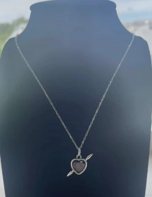 Silverhalsband med hjärthänge hjärta - Snyggt silverhalsband med ett hjärtformat hänge som har en pil genom sig. Kedjan är tunn och stilren, perfekt för att ge din look lite extra edge. Hänget har en mörkare ton i mitten som ger cool kontrast mot det blanka silvret.