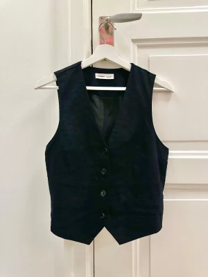 Svart väst - Svart väst i linne från Pull & Bear. Går att spänna i ryggen om man önskar en kroppsnära eller lösare look. Använd 1 gång så säljes i nyskick. 