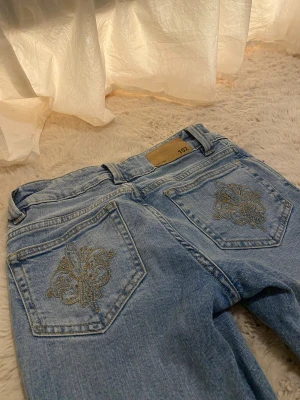 Bootcut jeans med broderi från Lager157 - Super snygga ljusblå bootcut jeans från Lager157 med guldfärgat broderi på bakfickorna. De har dragkedja och dubbla knappar fram. Jeansen har låg midja och är tillverkade i jeansmaterial med coola detaljer.