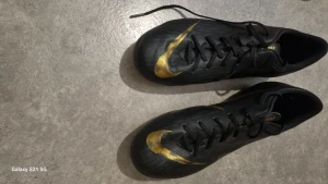 Svarta Nike fotbollsskor med gul detalj - Säljer ett par svarta Nike fotbollsskor med snygga guldfärgade swoosh-detaljer på sidan. Skorna har snörning och en smal, sportig form som passar perfekt för dig som gillar att spela fotboll. Materialet är syntet och designen är riktigt modern.