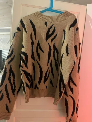 Beige stickad zebramönstrad tröja - Säljer en beige stickad tröja från NA-KD i storlek XS med svart zebramönster. Tröjan är i ett ganska så tjockt material