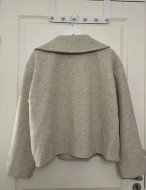 Beige skepparkavaj med stora slag - Säljer en beige skepparkavaj med breda slag och dubbelknäppning framtill. Jackan har svarta knappar både på framsidan och vid ärmsluten, samt en loose passform. Materialet är mjukt och känns som ull, perfekt för höst och vinter. Aldrig använd . Nypris 400