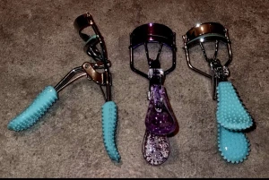 Tre ögonfransböjare med färgglada handtag - Säljer tre ögonfransböjare i metall med olika färgglada handtag. Två har turkosa, gummibeklädda handtag med knottrig yta för extra grepp, och en har ett lila transparent handtag med glitter. Perfekt för att få snygg böj på fransarna.