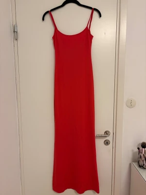 Röd långklänning från Bershka - Säljer en röd långklänning från Bershka med smala axelband och enkel, stilren design. Klänningen har en figurnära passform och är tillverkad i ett mjukt, stretchigt material som känns bekvämt mot huden. Perfekt för dig som gillar minimalistisk och trendig stil.