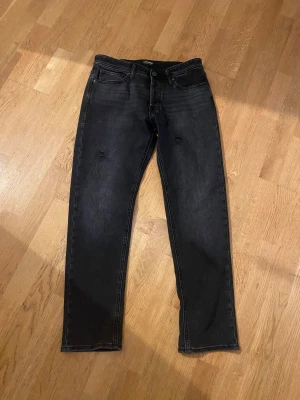 Svarta tapered jeans från Jack & Jones - Snygga svarta jeans från Jack & Jones med tapered fit och diskreta slitningar på låren. Jeansen är använda EN gång!! Jeansen är tillverkade i stretchig denim för skön passform och har en modern, smal siluett. Storleken är W31 och L32