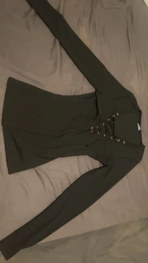 Svart långärmad topp med snörning - Säljer en svart långärmad topp med snygg snörning framtill och guldfärgade öljetter. Modellen är figurnära och har en enkel, stilren design som passar perfekt till jeans eller kjol. Toppens material känns mjukt och stretchigt.