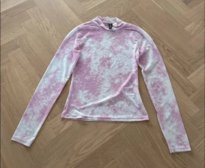 Rosa och vit långärmad polotröja H&M - Säljer en tunn och mjuk långärmad polotröja från H&M Divided i storlek S. Tröjan har ett snyggt batikmönster i rosa och vitt, med hög hals och figurnära passform. Perfekt att styla med jeans eller kjol för en cool look.