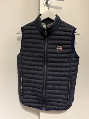 Mörkblå dunväst från Colmar - Snygg mörkblå dunväst från Colmar med quiltad design och horisontella sömmar. Västen har dragkedja framtill, två fickor med dragkedja och Colmar-logga på bröstet. Insidan är ljusgrå och materialet är lätt och smidigt, perfekt för lager-på-lager.