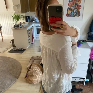 Vit blus med v-ringning från Dobber - Säljer en vit blus från Dobber med v-ringad hals och långa puffiga ärmar. Blusen har en lätt skrynklig struktur och tunna knytband framtill. Materialet känns mjukt och luftigt, perfekt för dig som gillar en chill och avslappnad stil.