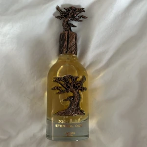 Lattafa Eternal Oud Eau de Parfum - Lattafa Eternal Oud Eau de Parfum 100 ml med unik flaska i glas och detaljer i bronsfärgad metall som föreställer ett träd. Parfymen har en lyxig känsla. Parfymen liknar mfk grand soir till 95% men med några mer noter som plommon. Sprutad 2 gånger så nästan helt ny. Nypris: 350.