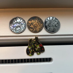 Pokemon pins och mynt i metall - Samlarpaket med tre Pokemon mynt i silver, guld och holografisk finish samt en färgglad Zygarde pin i svart, grönt och rött. Perfekt för dig som älskar Pokemon och vill ha snygga accessoarer till väskan eller jackan. Pris går att diskutera