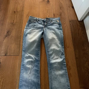 Replay ljusblå bootcut jeans - Snygga ljusblå jeans från Replay med bootcut passform. Jeansen har klassiska fem fickor, dekorativ broderad bakficka och ett rosa patch med blommor i midjan. Tillverkade i mjukt denim med slitningar för en cool look.