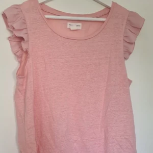 Rosa linnetopp med volangärmar - Supersöt ljusrosa linnetopp från Holly & Whyte med volangdetaljer på ärmarna. 