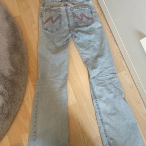 Dom virala Nelly jeansen - Säljer ett par ljusblå bootcut jeans med slitna knän och snygga röda broderier på bakfickorna. Jeansen har klassisk femficksdesign och är tillverkade i jeansmaterial. Perfekta för dig som gillar en avslappnad och trendig look.