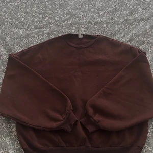 Oversized brun tröja fån Nelly - En basic mörkbrun sweatshirt från NELLY  i storlek XS. Tröjan har rund halsringning, ribbade muddar vid ärmslut och nederkant samt en loose passform. Perfekt för dig som gillar en enkel och stilren look.