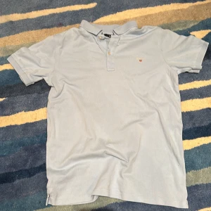 Ljusblå pikétröja från GANT - Säljer en klassisk ljusblå pikétröja från GANT med korta ärmar och krage. Tröjan har två knappar vid halsen och en liten broderad GANT-logga på bröstet. Perfekt för en clean och stilren look. Har inte kvar kvitto tyvärr.