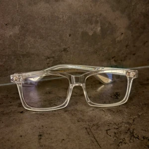 Transparenta Chrome Hearts glasögon - Snygga glasögon från Chrome Hearts med transparent båge och rektangulär form. Skalmarna har detaljerade silverfärgade mönster och logotyp. Perfekt för dig som vill sticka ut med en unik och modern stil.