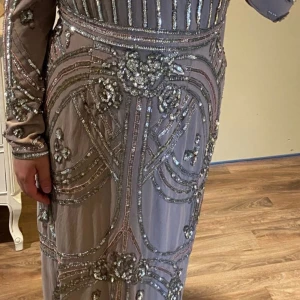 Champagnefärgad långklänning med paljetter - Säljer en elegant långklänning i champagnefärg med glittriga paljettdetaljer och broderade mönster. Klänningen har långa ärmar och är täckt av silvriga och glittriga dekorationer som ger en lyxig känsla. Perfekt för dig som vill sticka ut på bal eller fest.