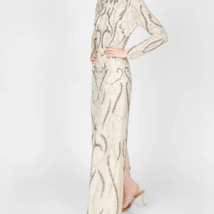 Glittrig långklänning i champagne - Säljer en elegant långklänning i champagnefärg med glittriga silverdetaljer och mönster. Klänningen har långa ärmar, figurnära passform och är täckt av paljetter som ger en lyxig känsla. Perfekt för bal eller nyår!