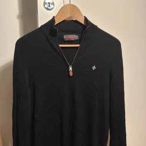 Svart merinoullströja från Morris - Säljer en svart långärmad tröja från Morris i 100% merinoull. Tröjan har en halv dragkedja framtill och en liten broderad logga på bröstet. Perfekt för dig som gillar stilrena och klassiska plagg med snygga detaljer. Nypris ligger på 1800 kr!