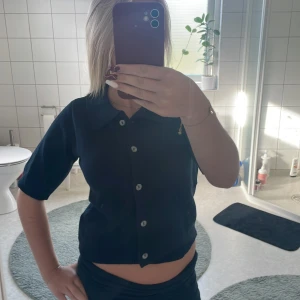 Mörkblå stickad blus från 157 - Säljer en mörkblå stickad blus från 157 med korta ärmar, klassisk krage och knappar framtill. Modellen är croppad och har en mjuk, ribbad känsla. Perfekt till jeans eller kjol. Aldrig använd!! Ny utan prislapp 🩷🩷